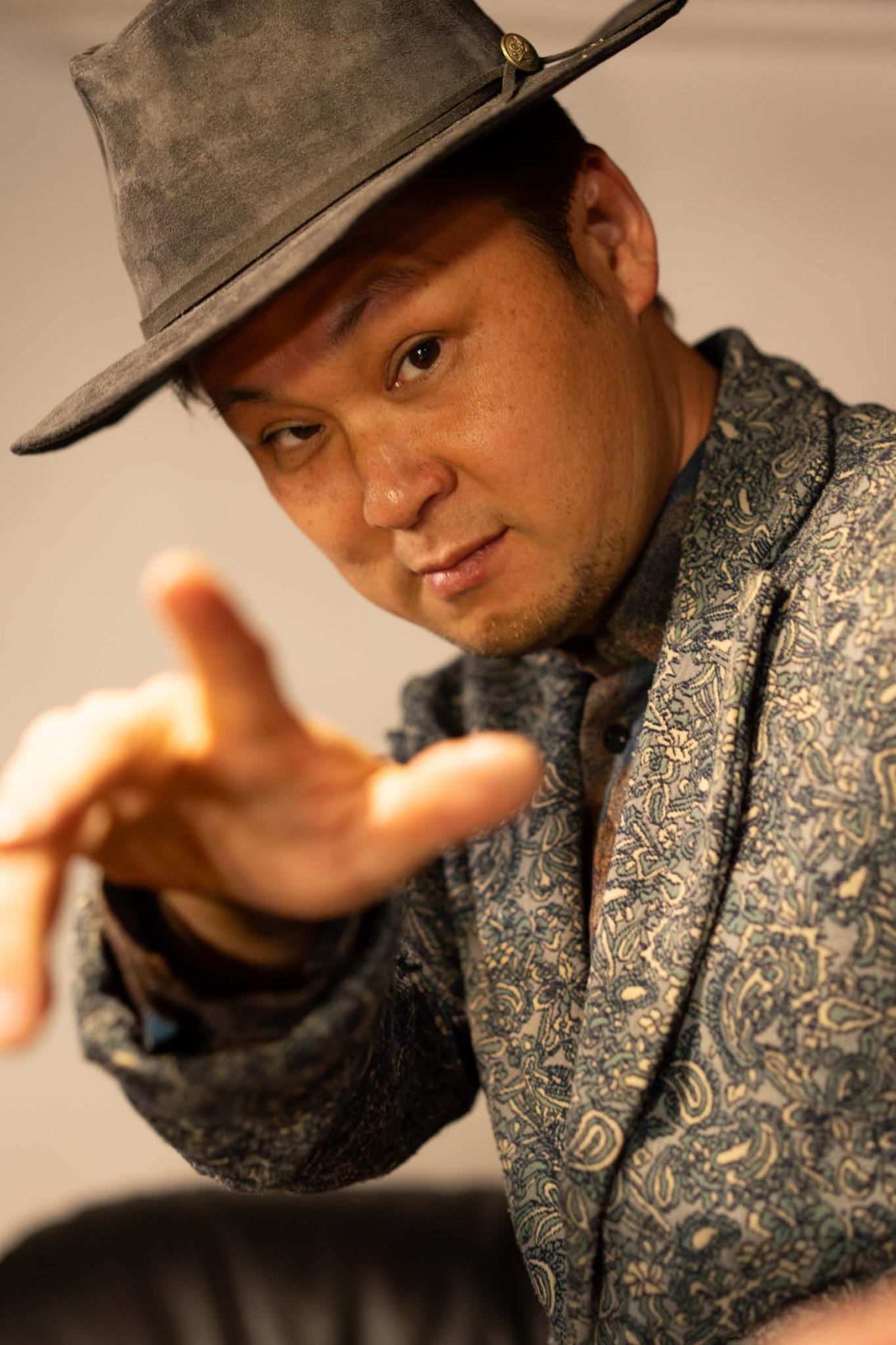 帽子をかぶり、カメラへ手を伸ばすポーズ